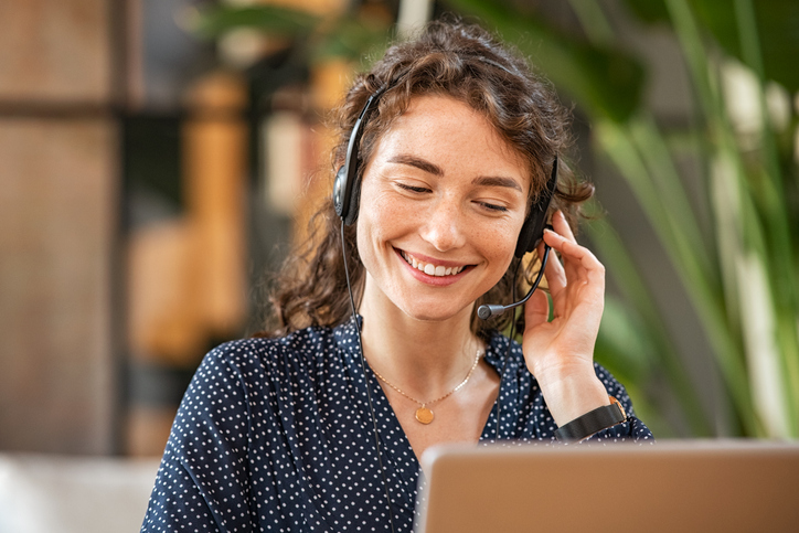 Happy young woman working on laptop while talking to customer on phone. Consulting corporate client in conversation with customer using computer. Service desk consultant talking in a call center.